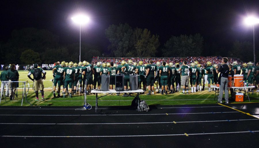 The West High football team stand on the sidelines before the marching band performance.