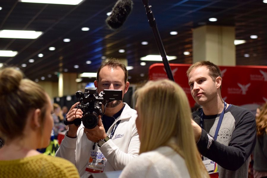 Two journalists video record a group of high school journalism students about their yearbook.