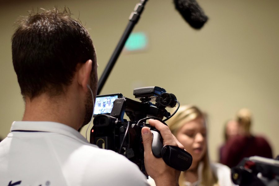 A journalist videotapes an interview.