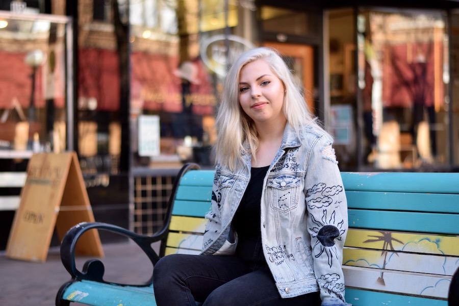 Maddie Molina '19 sits on a bench in downtown Iowa City, showing her outfit (jacket from American Eagle, shirt from American Apparel, jeans from American Eagle, paired with Adidas Superstars)