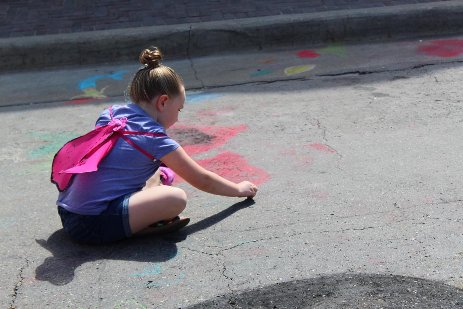 A girl chalks a picture on the pavement. Everywhere on the street, kids and adults were creating chalk art.