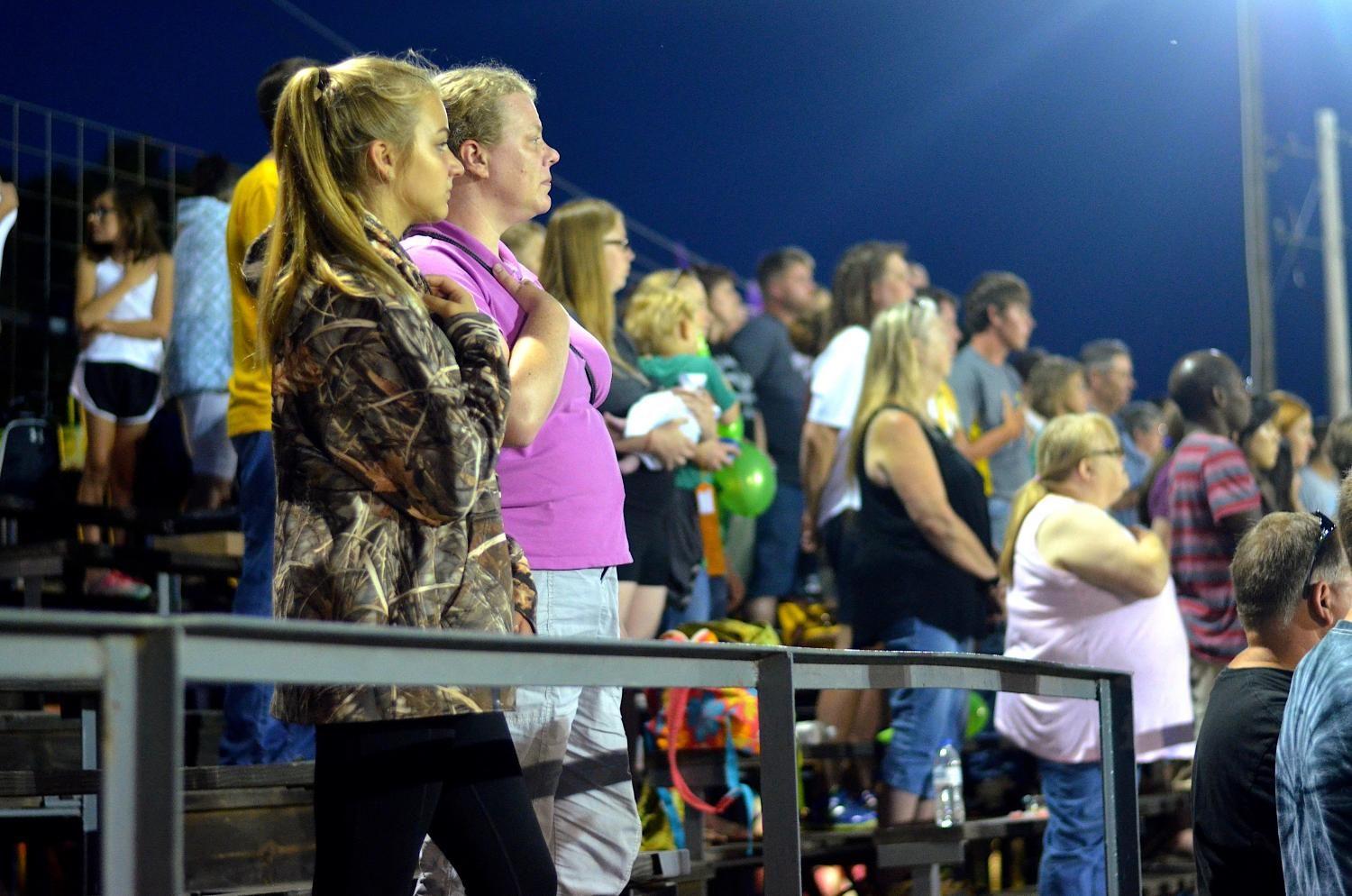 Members of the crowd stand to salute the Color Guard and the playing of the national anthem on at the Johnson County Fair on July 27 in Iowa City.