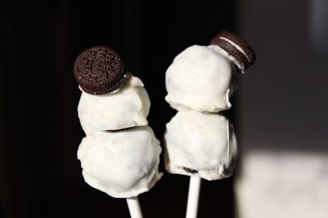 The completed cake balls have been dipped in the melted white chocolate and stacked onto skewers, using mini Oreos as the hats of the cake ball snowmen.
