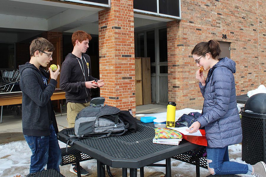 Liam Edberg 22, Tony Abdel Malek 22 and Claire Loussaert 22 eat lunch outside with a layer of snow on the ground on Friday, Nov. 30. The group has resorted to standing around a table while eating lunch because the benches are too cold. 