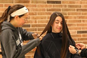 Anna Moore 21 watches Julia Bernat 21 cut a strand of Moore’s hair after school in the commons during the annual West High School Dance Marathon hair drive on Jan. 11. “I had wanted to cut my hair for a few months,” Moore said. “[I] waited until the West High Dance Marathon hair drive because I knew people who had donated their hair in the past and I thought it sounded like a cool way to help out. It’s a little thing to do for a great cause.”