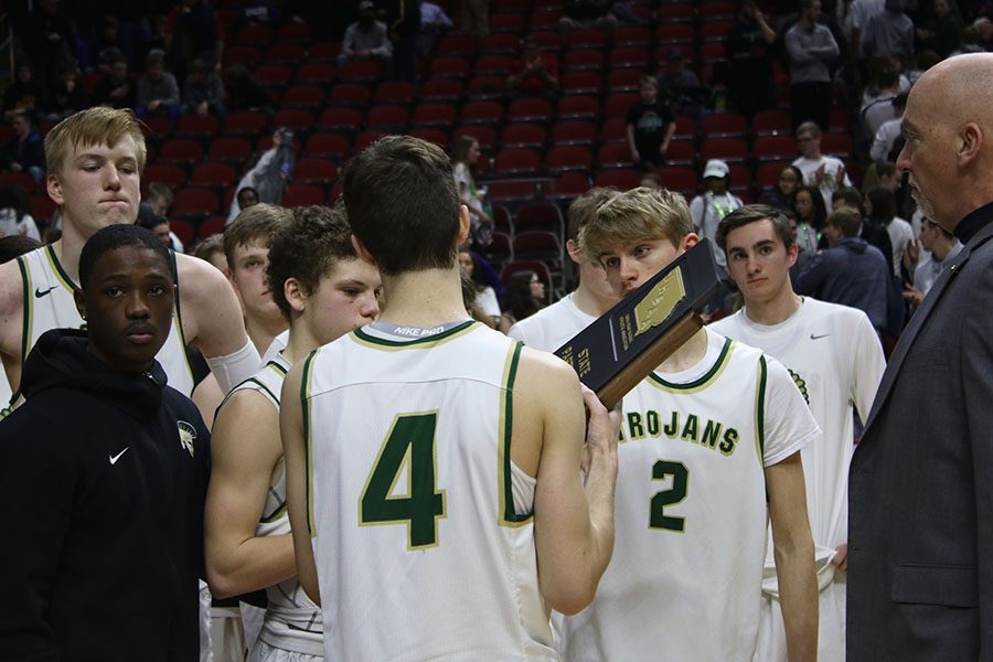 The boys basketball team huddles around their trophy for participating in the state tournament on Wednesday, March 6.