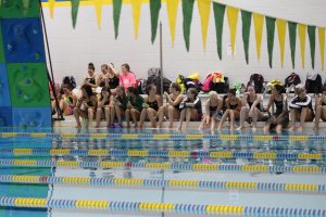 Members of the West High swim team sit as a team to watch the diving portion of the meet on Sept. 17, 2019. 