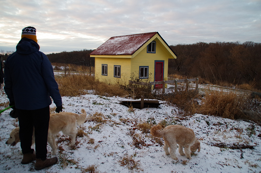 Karen Meyer and her dogs outside of a small playhouse for kids at Harvest Preserve.