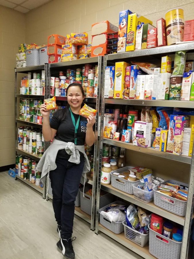 Omega Dancel poses with packets of ramen in front of shelves of food. 