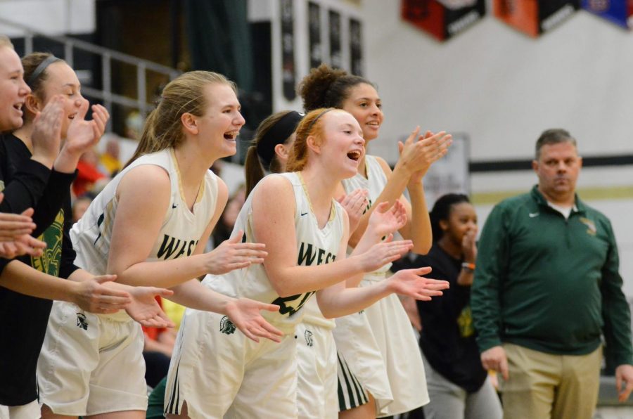 Liv Williams 21, Rylee Goodfellow 21, and Ana Prouty 23 cheer from the bench as Matayia Tellis makes a shot and gets two free throws off of a foul. 