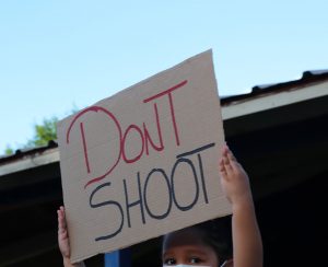 A little girl holds up a sign for the crowd to see, possessing the words Dont Shoot.