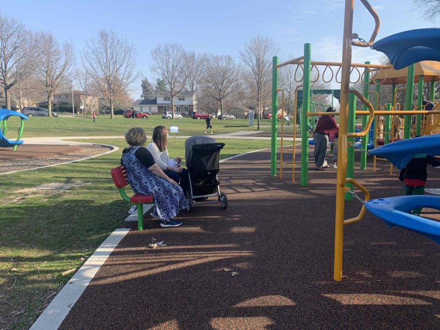 On a beautiful sunny day, a mother and her daughter visit Willow Creek Park wearing their masks. Theyre both seated on the bench, and the daughter is holding her infant son to keep him from crying as the mother looks around the park.