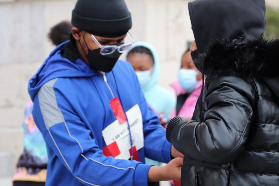 A student helps a peer tape a protest sign to their coat at the protest on 11/19/21