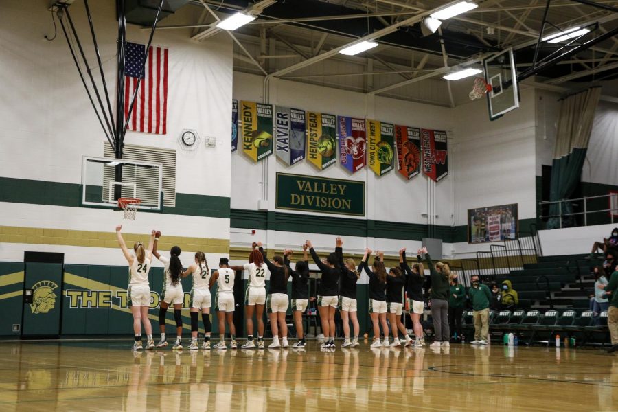 The girls basketball team raises their hands at the end of the national anthem before facing off with Cedar Rapids Washington on Dec. 3.