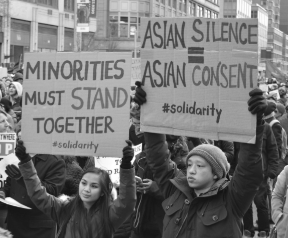People are holding signs at a protest urging other Asian Amerians to support the community and other minorities. 