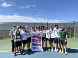 The boys tennis team musters up the strength to hold Seth Smigel 25 for a photo with their championship trophy and banner after the conclusion of team state at the Prairie Ridge Sports Complex on May 31.