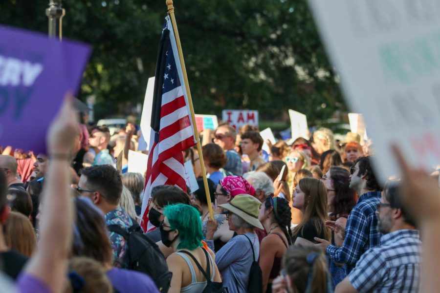 A protester stands in a swarm of signs holding up and American flag at the Protest on the Pentacrest on June 24, 2022. 