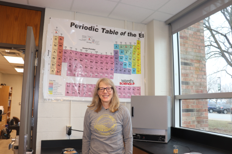 Michelle Wikner stands in front of a poster of the periodic table 