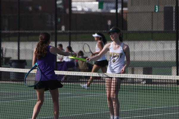 Audrey Crawford ’26 meets her opponent at the net to exchange balls before switching sides at the girls tennis meet on the West High tennis courts April 18.