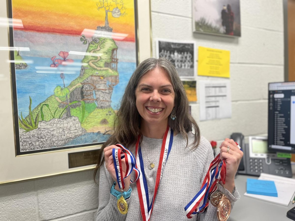 Guidance secretary and assistant cross country coach Brittany McConnell stands beside her desk while holding running medals she earned decades ago. 