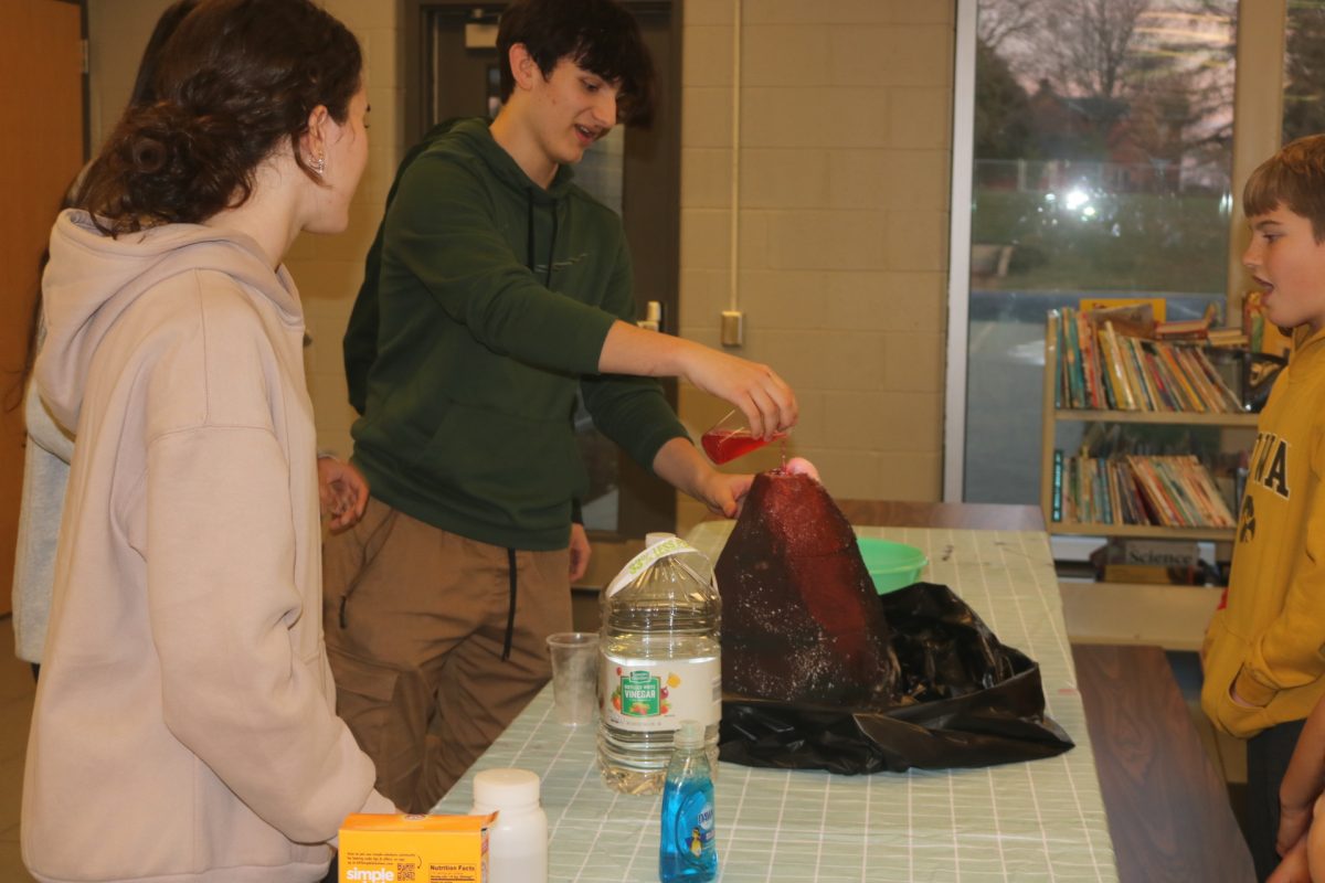 Sawyer Smith 25 pours vinegar into the model volcano while students watch. 