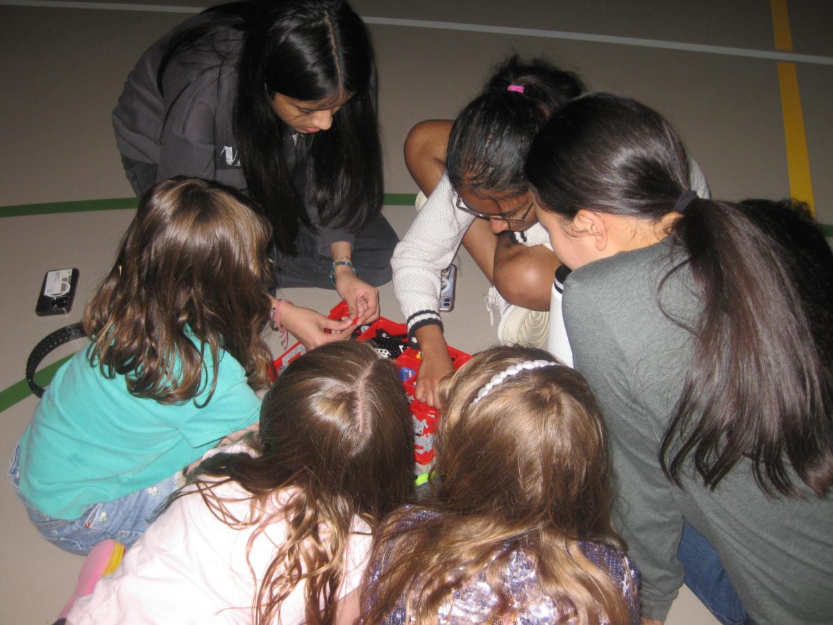 Shanza Sami '26, Aahana Gupta '27 and Erin Chen '27 help a group of students find LEGO pieces. 