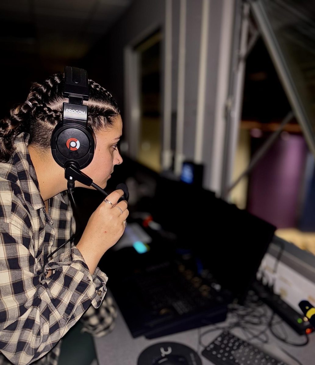 Genna Ray '25 speaks into her headset while looking down at the stage. 