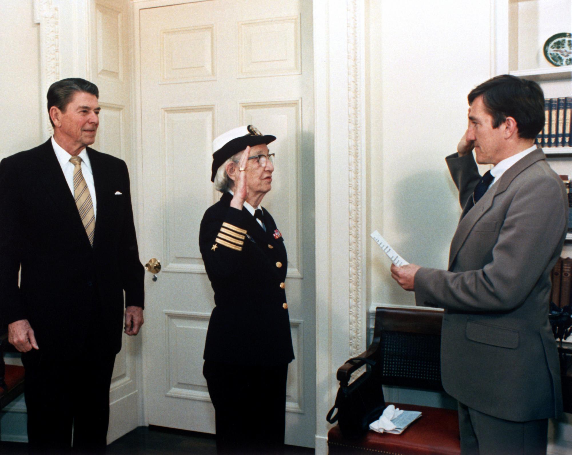 Secretary of the Navy, John Lehman, right, promotes Capt. Grace Hopper to the rank of Commodore in a ceremony at the White House. President Ronald Reagan is at the left.