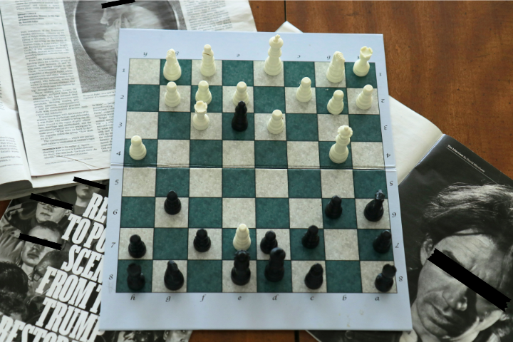 A chess board surrounded by magazines shows a checkmate- with the white pieces in control of the board.