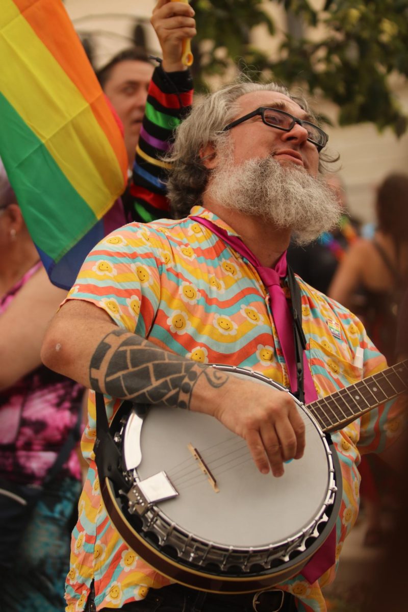Ignoring counter-protesters at Iowa City's Pride Parade on June 15, 2024, a man plays a banjo, surrounded by pride flags.