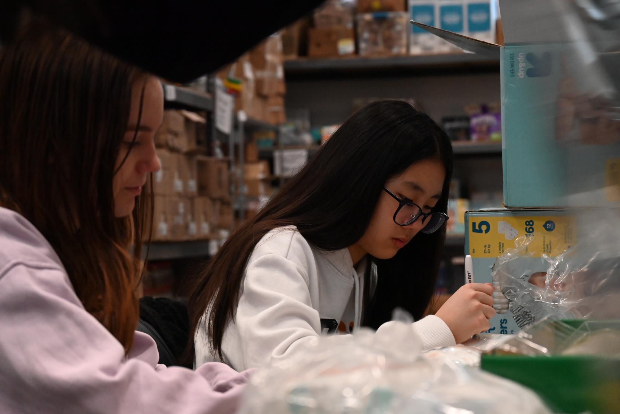Cora Beland ’29 and Youan Lee ’29 package diapers at the Coralville Food Pantry. The diapers are taken out of boxes and grouped into seven, then wrapped up to be given to community members.